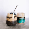 Chia pudding layered with All Natural Macadamia Nut Butter in a glass, topped with House of Macadamias All Natural Macadamia Nut Butter layered in chia pudding with blueberries and banana slices in a glass and banana slices
