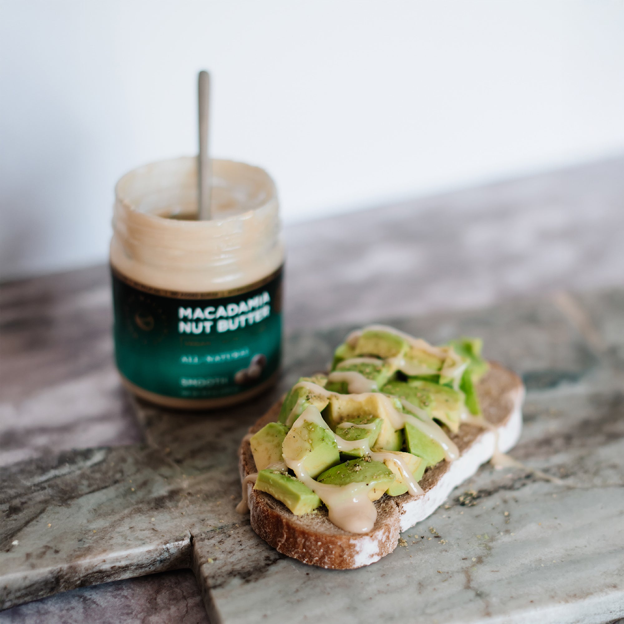 House of Macadamias Sourdough toast topped with avocado and a drizzle of All Natural Macadamia Nut Butter, served beside the nut butter jar
