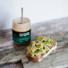 House of Macadamias Sourdough toast topped with avocado and a drizzle of All Natural Macadamia Nut Butter, served beside the nut butter jar