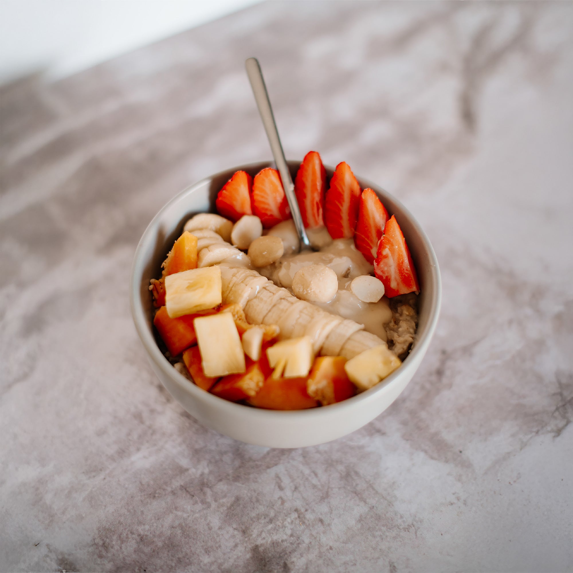 Fruit bowl with banana, strawberry, papaya, pineapple, oats, macadamia nuts, and All Natural Macadamia Nut Butter drizzled on top