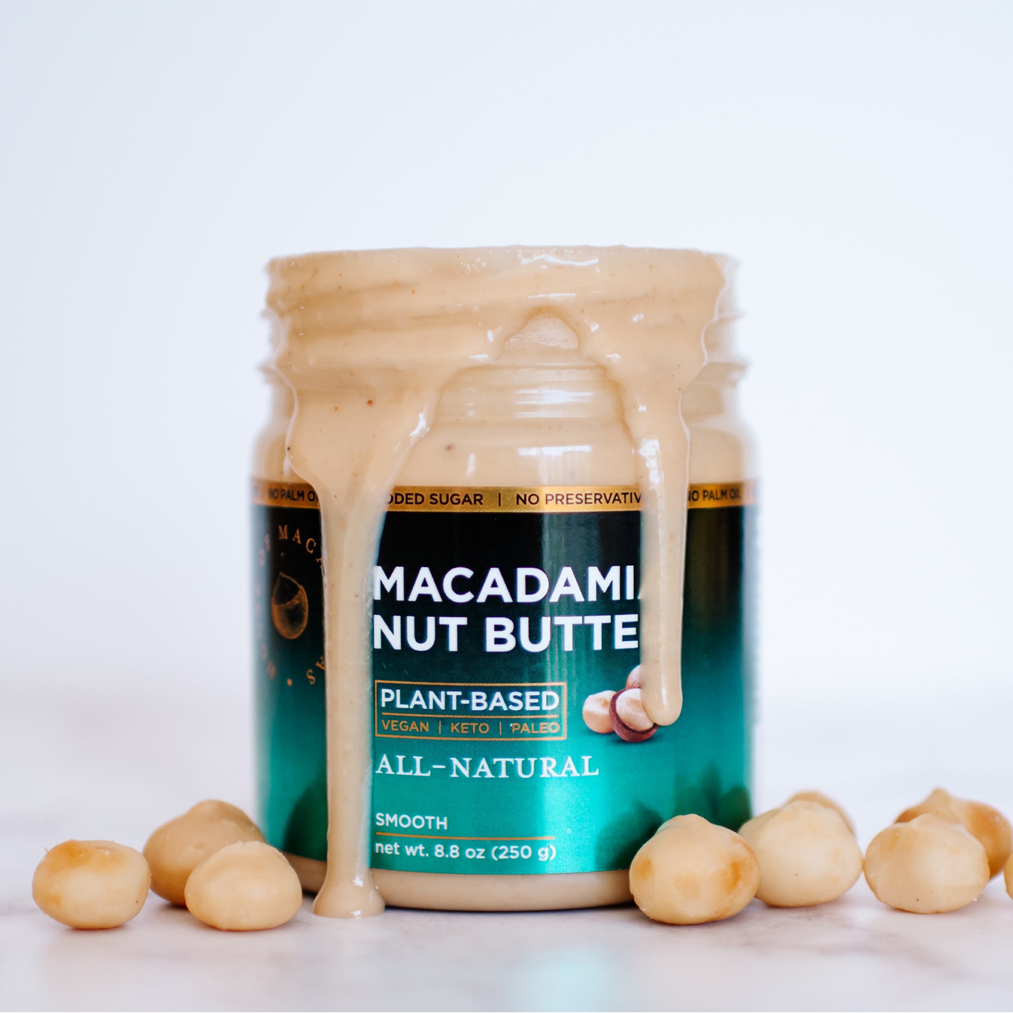 House of Macadamias All Natural Macadamia Nut Butter jar with whole macadamia nuts beside it on a white background