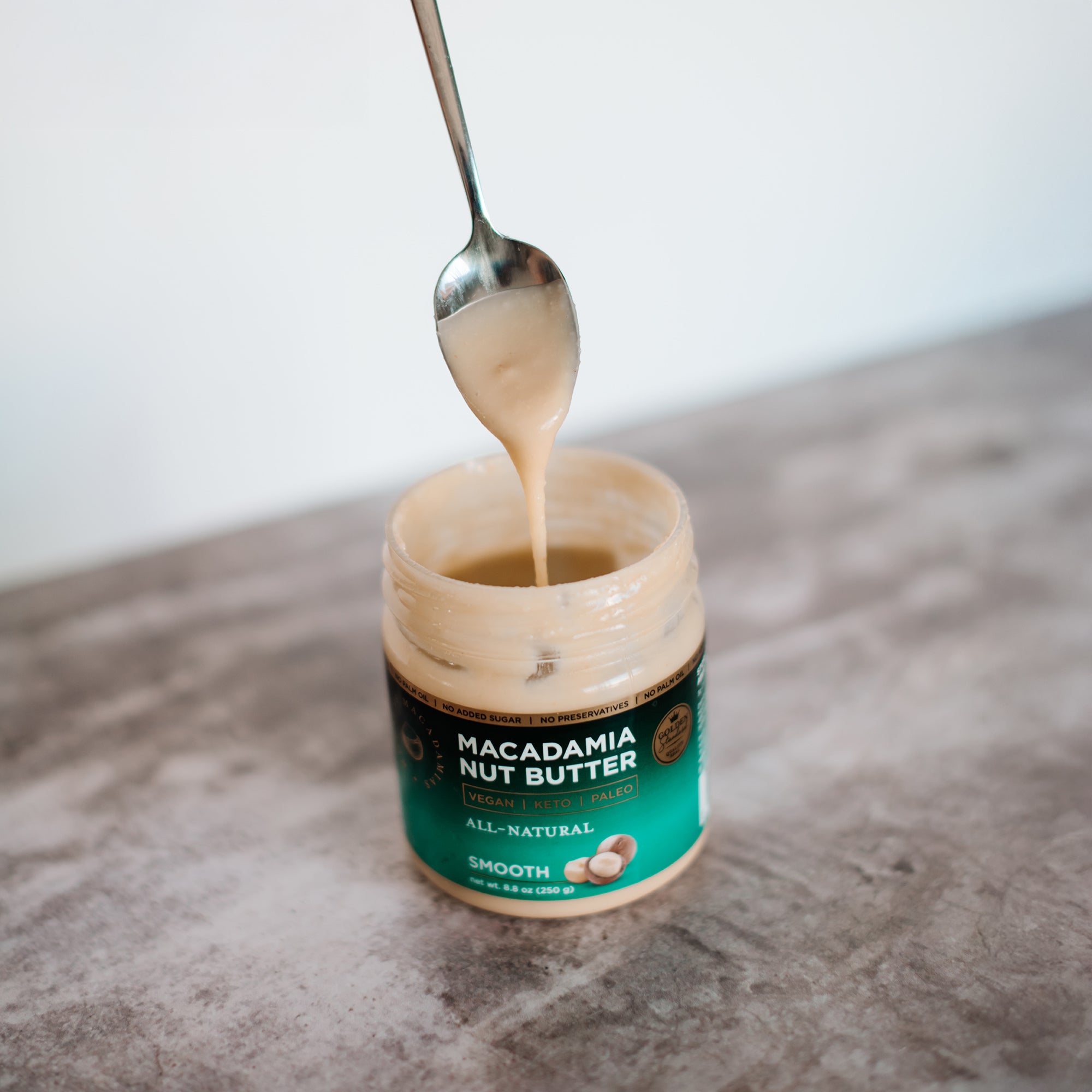 House of Macadamias All Natural Macadamia Nut Butter jar with a spoon drizzling nut butter back into it
