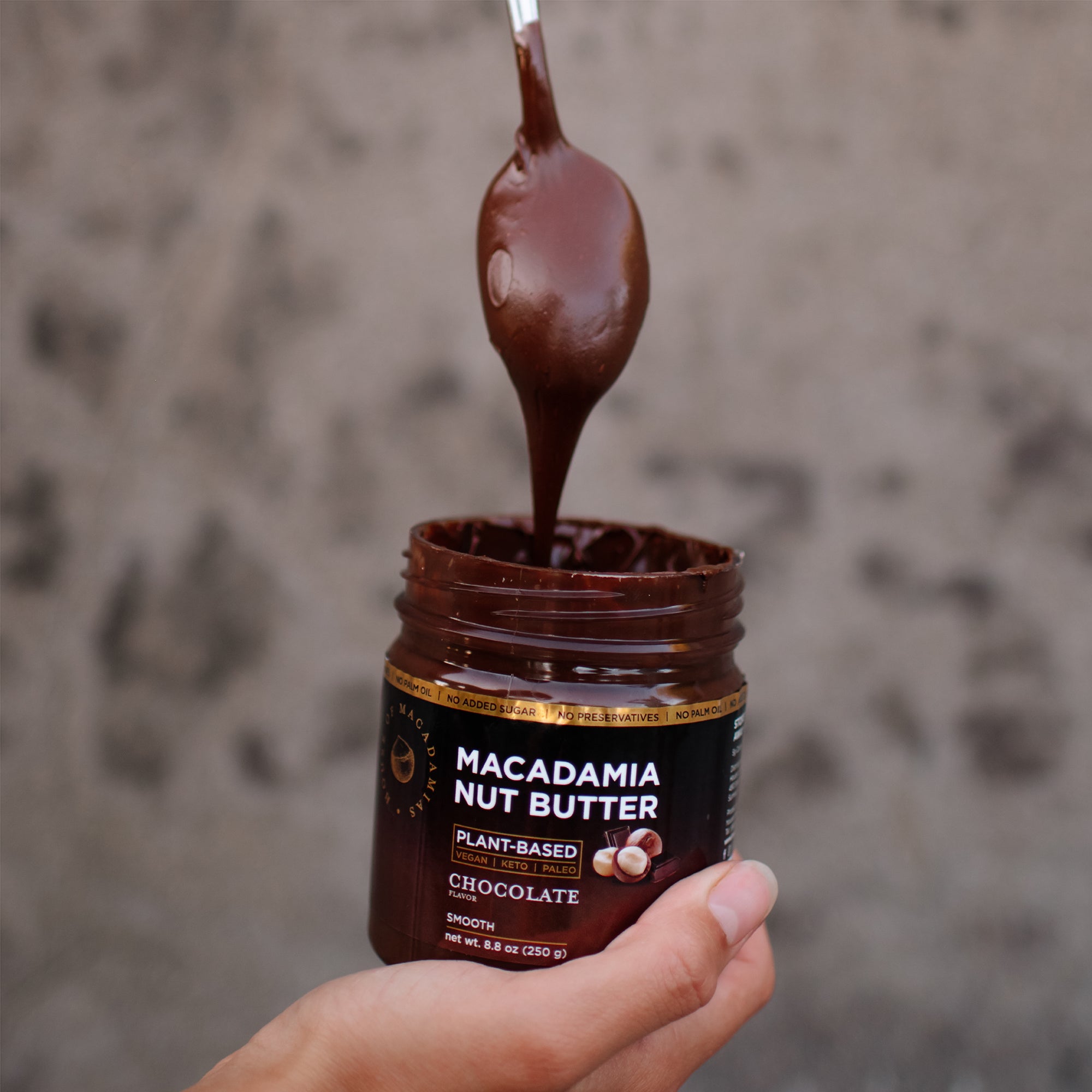 House of Macadamias Chocolate Macadamia Nut Butter dripping from a spoon into the jar, showcasing creamy texture and rich in healthy monounsaturated fats