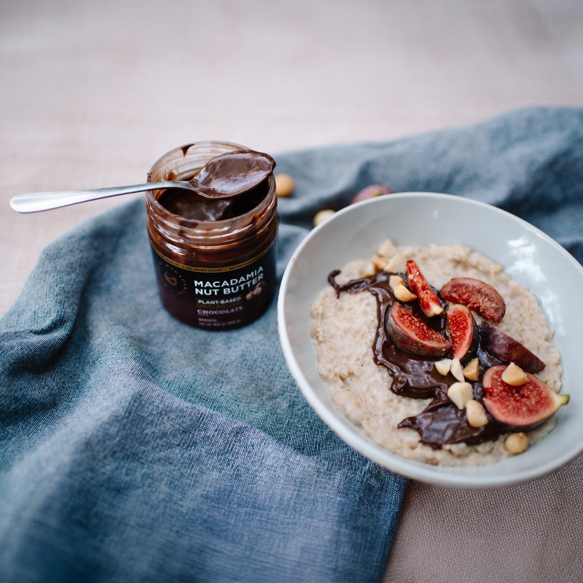 House of Macadamias Chocolate Macadamia Nut Butter next to a bowl of oats topped with fruit and nut butter, garnished with whole macadamia nuts — a nutritious and wholesome breakfast option