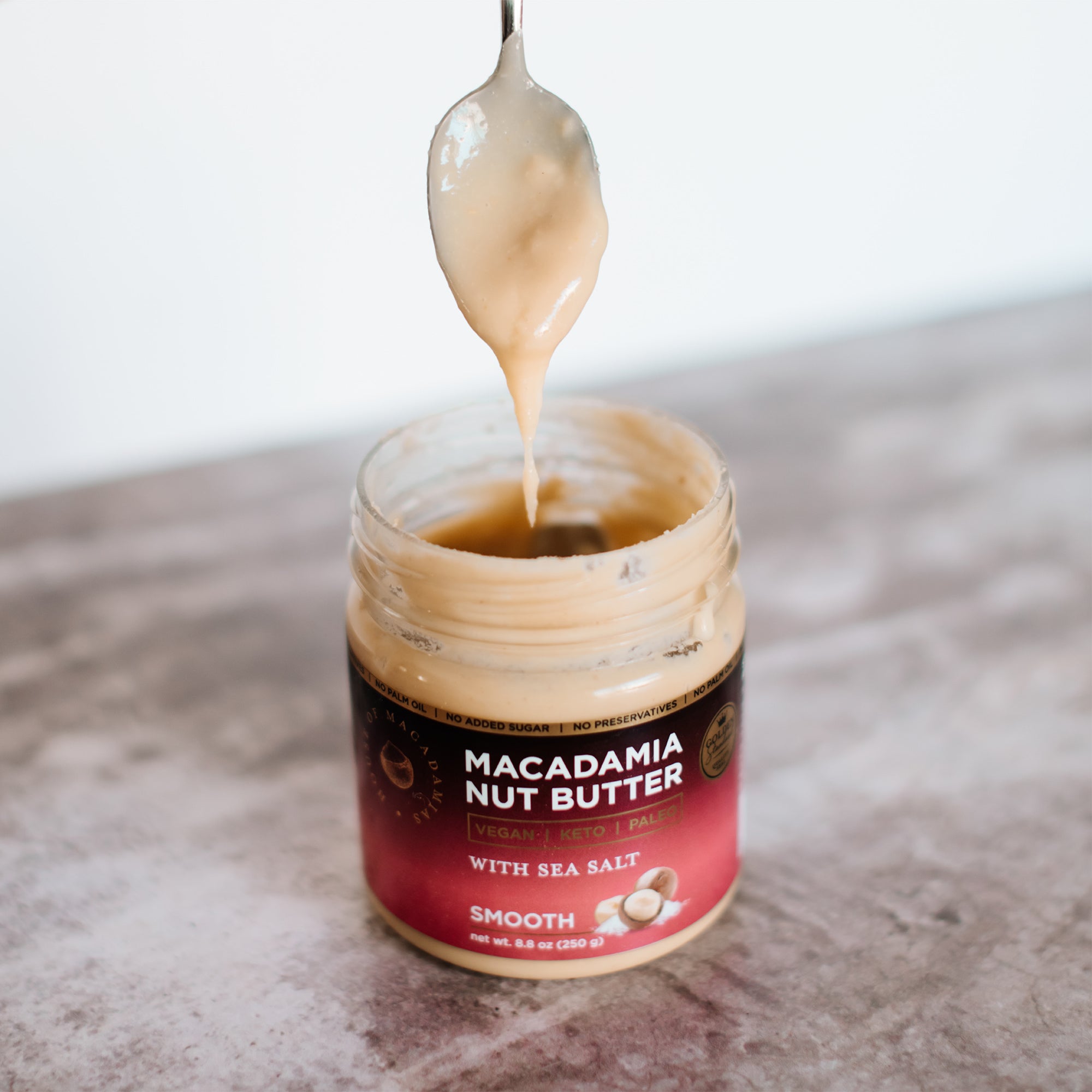 House of Macadamias Sea Salt Macadamia Nut Butter jar with a spoon dripping nut butter into it