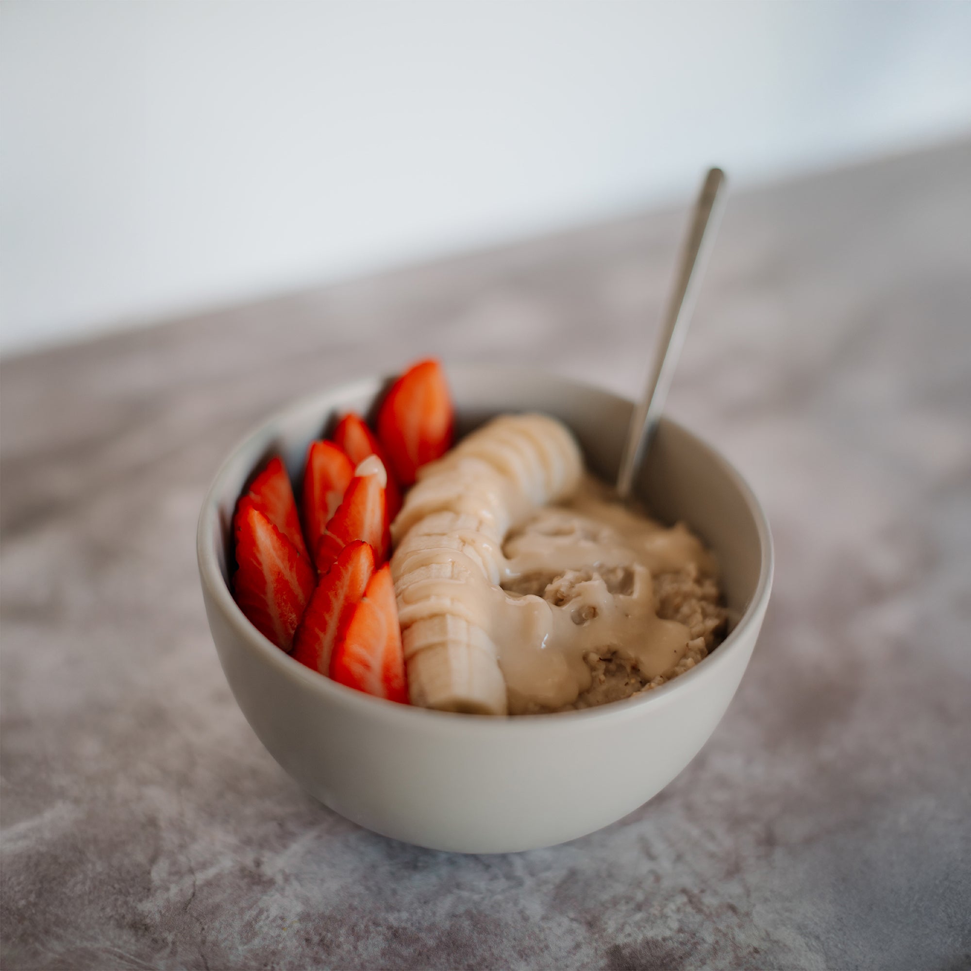 House of Macadamias Sea Salt Macadamia Nut Butter drizzled over a nutritious fruit bowl with strawberries, banana, and oats — a healthy, clean-ingredient snack
